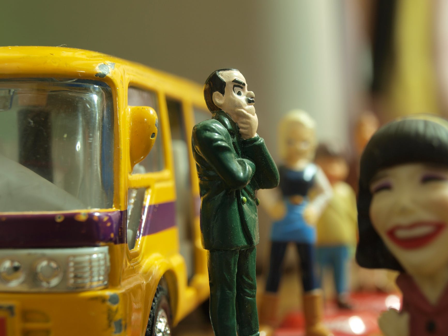 man in green coat figure standing in front of yellow toy bus